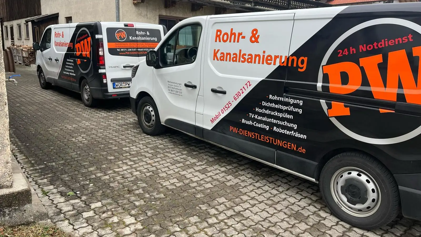 Zwei Einsatzfahrzeuge der PW Rohrreinigungs GmbH mit Leistungsliste auf einem gepflasterten Hof